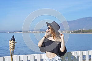 Woman traveling talking on the phone, cute girl smile, on background of the sea / ocean. The concept of connection and communicati