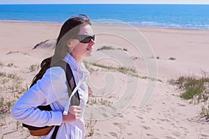 Woman traveller with backpack is looking around in sea sand beach on vacation.