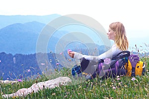 Woman Traveller with backpack sitting on grass with flowers relaxing