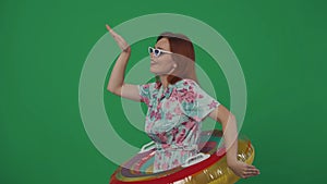 Woman traveller in glasses dancing wearing inflatable tube ring, smiling and happy face expression. Isolated on green