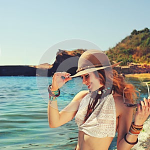 Woman traveller hiking near the sea beach, smiling and beautiful, dressed in boho chic bracelets and hat,