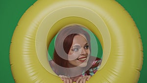 Woman traveller holds big yellow inflatable tube ring and looking through it with amazed smiling face expression