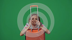 Woman traveller looking through suitcase holder, smiling at the camera, happy face expression. Isolated on green