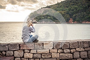 Woman traveller making mobile photo of picturesque landscape during travel holidays sitting on old wall during sunset at beach