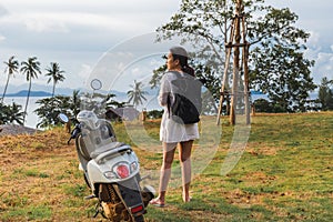 Woman traveller standing near motorcycle on the tropical beach.