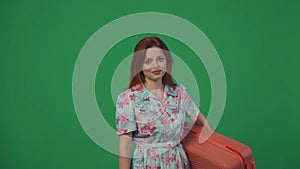 Woman traveller standing posing with suitcase, looking at the camera smiling face. Isolated on green background.