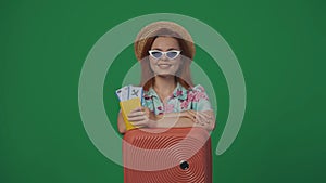 Woman traveller in straw hat and glasses with suitcase holding flight tickets, passport and smiling. Isolated on green