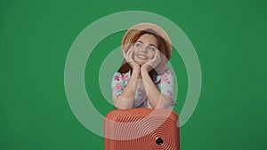 Woman traveller in straw hat with happy smiling face expression dreaming, hands on suitcase. Isolated on green