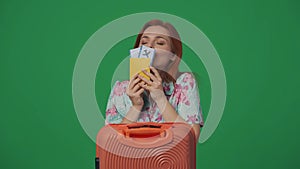 Woman traveller with suitcase holding flight tickets, happy smiling face expression, kissing the tickets. Isolated on