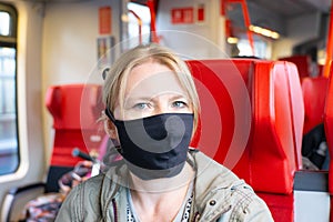 Woman travelling in a railway train wearing a self made face mask. Coronavirus and travel concept