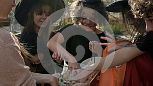 Woman treats sweets to a group of children in black fancy dress with scary makeup on their faces. Halloween traditions.