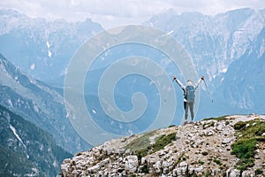 Woman trekker with backpack rose arms up with trekking poles enjoying picturesque Dolomite Alps view near Tre Cime di Lavaredo