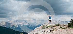 Woman trekker with backpack rose arms up with trekking poles enjoying picturesque Dolomite Alps view near Tre Cime di Lavaredo