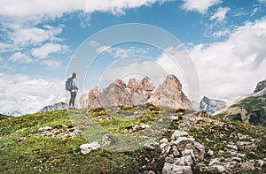 Woman trekker with backpack and trekking poles on green hill enjoying picturesque Dolomite Alps view near Tre Cime di Lavaredo