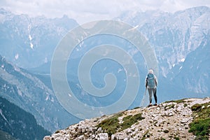 Woman trekker with backpack and trekking poles on the hill enjoying picturesque Dolomite Alps view near Tre Cime di Lavaredo