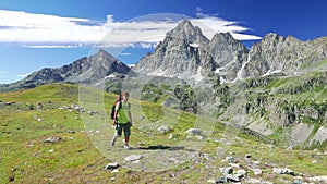 Woman trekking in idyllic mountain landscape on footpath crossing blooming green meadow set amid high altitude rocky mountain