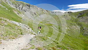 Woman trekking in idyllic mountain landscape on footpath crossing blooming green meadow set amid high altitude rocky mountain