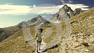 Woman trekking in idyllic mountain landscape on footpath crossing blooming green meadow set amid high altitude rocky mountain rang