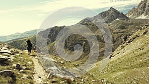 Woman trekking in idyllic mountain landscape on footpath crossing blooming green meadow set amid high altitude rocky mountain rang