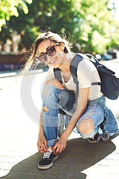 Woman in a trendy clothes fastens sneakers on the street