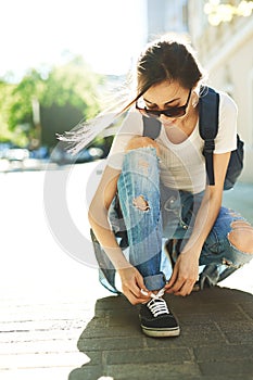Woman in a trendy clothes fastens sneakers on the street
