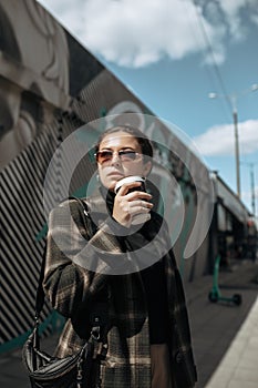 Woman in trendy clothes and in sunglasses with paper cup coffee