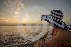 Woman in a trendy straw sunhat relaxing on a beach looking out o