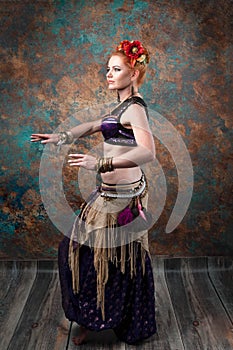 woman in tribal costume with black lace top and purple pants in red circlet of flowers standing in dance pose