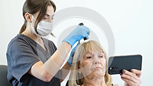 A woman trichologist works with a client in a modern clinic. Scalp cleaning using a dermatoscope.