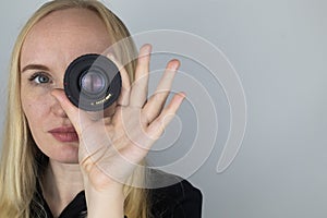A woman tries on a camera lens instead of an eye. The concept of the photographer`s work and the creative approach to photography