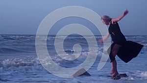Woman tries keep her balance, standing on a stone on one leg, in sea, falls, laughs