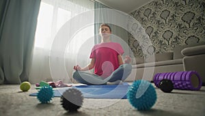 A woman tries to meditate at home among sports equipment.