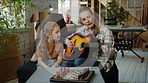 A woman tries to play the guitar, listens to the sound and communicates with her daughter