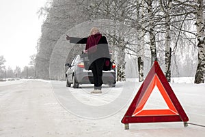 A woman tries to stop a car on a winter road. Sign on an emergency stop.