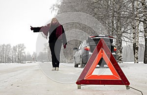 A woman tries to stop a car on a winter road. Sign on an emergency stop.