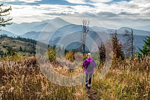 Woman with trekking poles hiking in autumn mountains