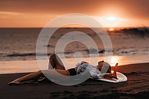 woman on tropical beach holding surfboard at sunset