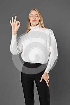 Woman in trousers and sweater shows OK gesture