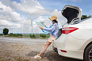 Woman in the trunk of a car looking at a map to reach the holiday destination with blue sky