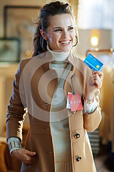 Woman trying coat with sale price tag and holding credit card
