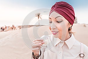 Woman with turban tasting arabian coffee while having tour and excursion in midlle eastern desert