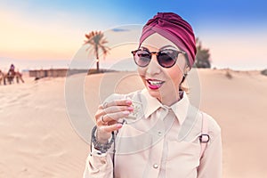 Woman with turban tasting arabian coffee while having tour and excursion in midlle eastern desert photo