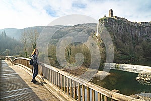 Woman turist poses on the old wooden bridge opposite impressive cliff village Castellfullit de la Roca