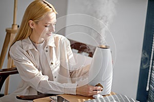 Woman turn on aroma oil diffuser on the table at home, steam from humidifier