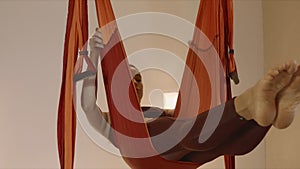 Woman turning body in air at studio. Gymnast performing aero yoga indoors