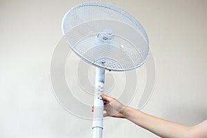 Woman is turning on Metal white modern fan or vent. Working electric floor standing fan in the house. Sunny hot summer day.