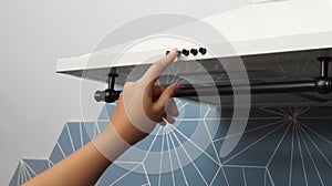 Woman turning on modern electric exhaust hood in kitchen, closeup