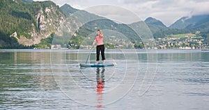 Woman turns SUP board around at Wolfgang lake Wolfgangsee, Austria, early morning, with mountains in the back.