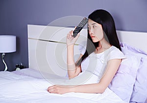 Woman with tv remote control on bed in bedroom