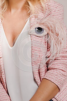 A woman in a tweed jacket with an eye-shaped brooch soft pink color